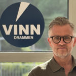Terje Wårheim står foran vindu med Vinn-logo. Han har briller på seg og hlder opp tommelen