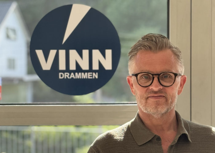 Terje Wårheim står foran vindu med Vinn-logo. Han har briller på seg og hlder opp tommelen
