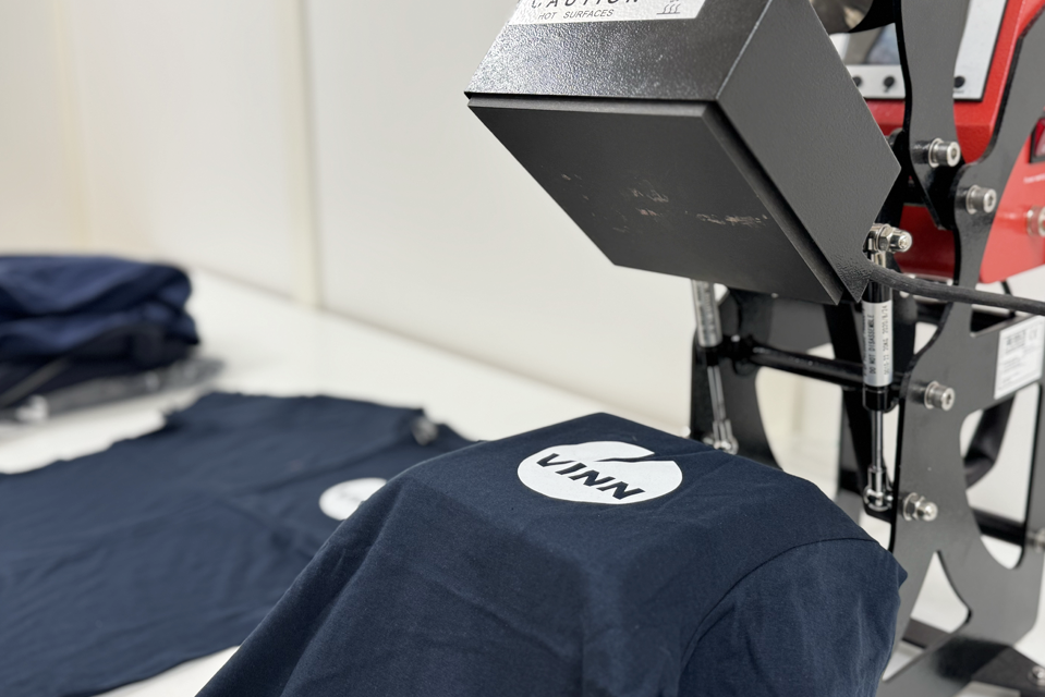 blå t-skjorte liggende på en tekstilpresse med en vinnlogo som skal settes på